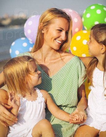 Happy woman and her little daughters at the beach with ballons. Mother day or birthday concept
