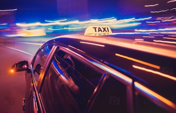 Taxi taking a left turn at night in an urban surrounding, seen from the rear end of the cab