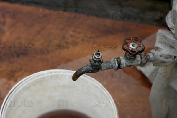 The picture of the old rusty water tap, crocked film. Under the tap is a plastic bucket with dirty water, stock photo