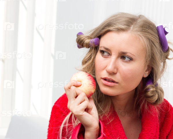 Girl in a red robe and curlers eating an apple, stock photo