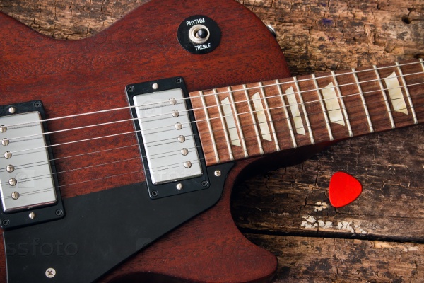 Les Paul electric guitar with a pick on a red wooden background