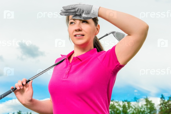 portrait of a girl with a golf club looking out for the flight path of the ball