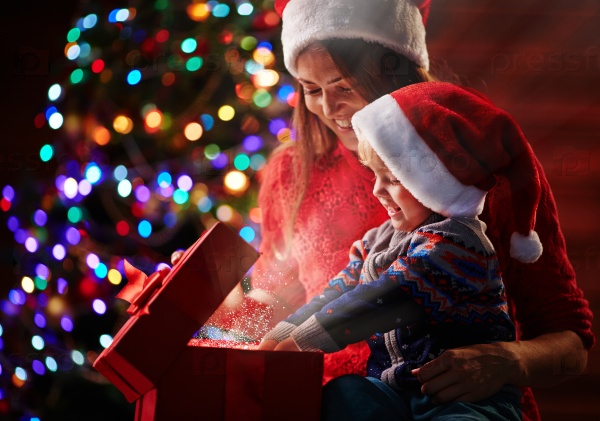 Happy woman looking at her son putting his hands into magic red giftbox with golden dust