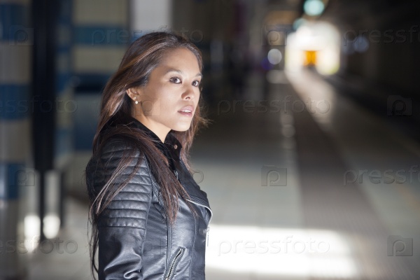 Pretty Asian woman, standing in an underground train station, looking around, waiting for her train to arrive at the platform