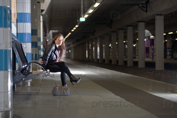 Young woman, sitting on a bench in an underground sation, waiting for her train to arrive at the platform