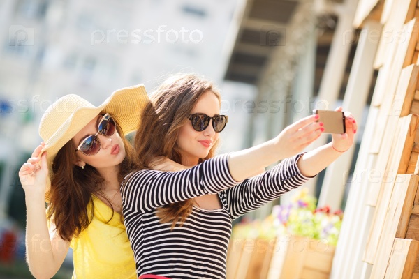 Friends making selfie. Two beautiful young women making selfie using smart phone, Friends making selfie. Two beautiful young women making selfie and grimacing in the city street.