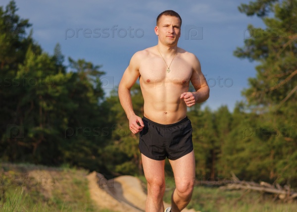 Young muscular man jogging outdoors on a summer evening.