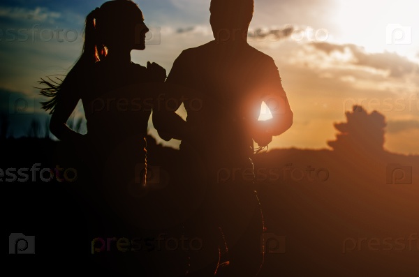 Young couple running at sunset outdoors. Solar flare illuminates a couple back.
