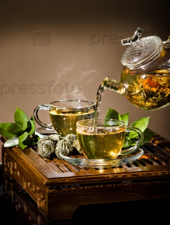 vertical photo, of the glass teapot flow green tea in cup on brown background,  tea ceremony