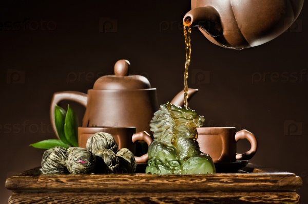 vertical photo, of the clay teapot tea flow in  cup on brown background,  tea ceremony