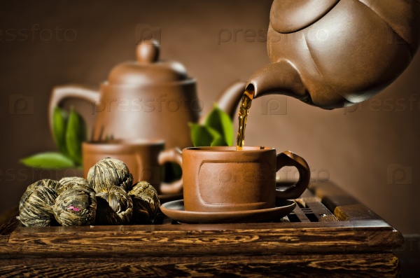 horizontal photo, of the clay teapot tea flow in  cup on brown background,  tea ceremony