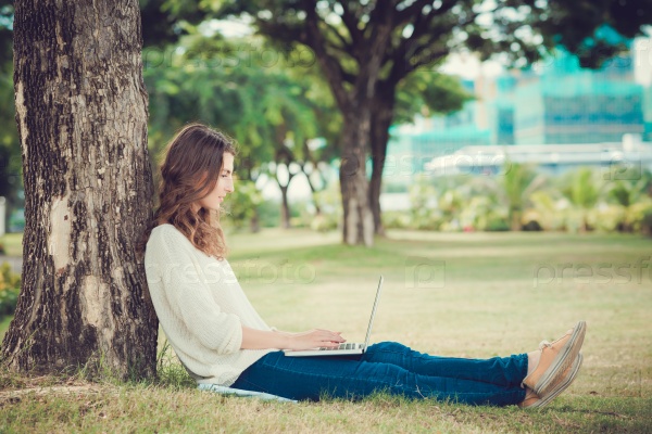 Copywriter with a laptop sitting under the tree and working on article