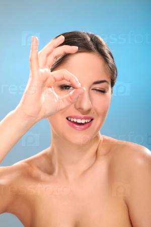 Caucasian woman with natural make-up shows ok isolated over blue background, stock photo