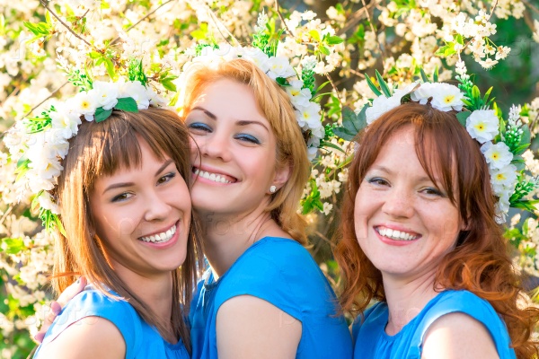 Three friends with wreaths on the head near the blossoming cherry in the park, stock photo