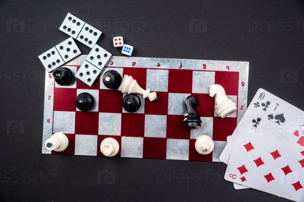 Various board games and figurines over checkers board and dark background. Metaphor for gaming and gambling.