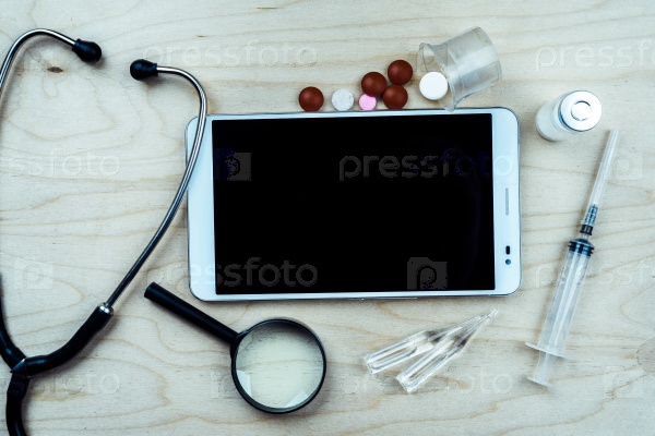 Tablet pc with medical objects on a desk as a metaphor for electronic diagnostic or healthcare mobile apps. Medical background