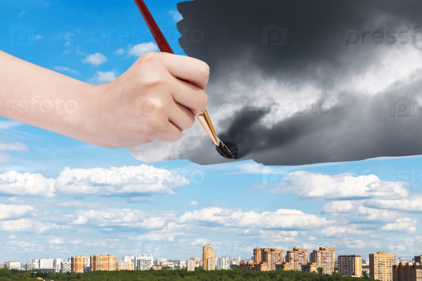 nature concept - seasons and weather changing: hand with paintbrush paints storm clouds over sunny city