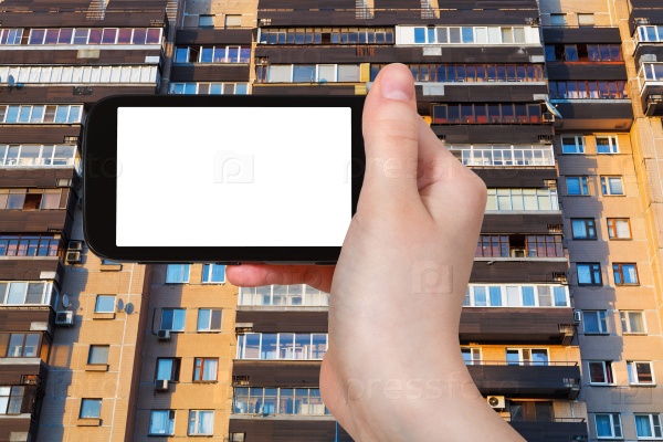 Travel concept - hand holds smartphone with cut out screen and facade on apartment house in Moscow on background, stock photo