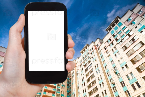 Travel concept - hand holds smartphone with cut out screen and new apartment houses on background, stock photo