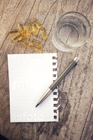 Blank notepad and pen with cod liver oil capsules on table