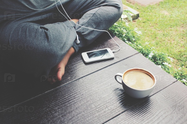 Woman playing smartphone with earphone and coffee in the garden