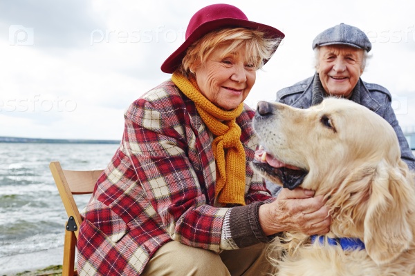 Retired woman cuddling cute pet with her husband on background