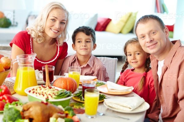 Happy young family sitting at celebration table on Thanksgiving Day and looking at camera