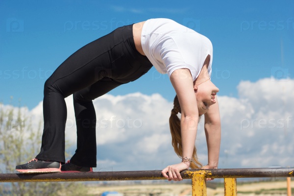 Athletic gymnast girl doing stretching exercise outside near horizontal bar after running, spring time, stock photo
