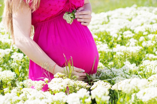 Happy smiling pregnant woman is wearing pink holding her belly