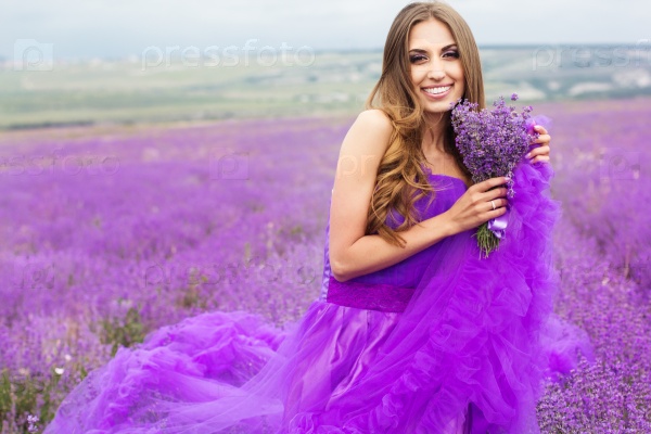 Beautiful sexy woman is wearing princess purple fashion dress posing at field of purple lavender flowers