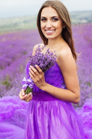 Beautiful sexy woman is wearing princess purple fashion dress posing at field of purple lavender flowers