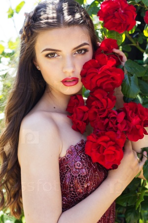 Closeup portrait of beautiful young fashion woman with red lipstick posing near roses in a garden