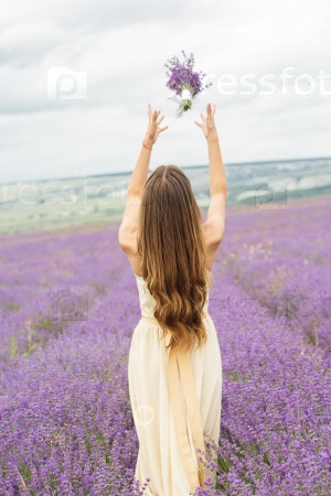 Back view of woman is wearing nice wedding dress standing at field of purple lavender flowers