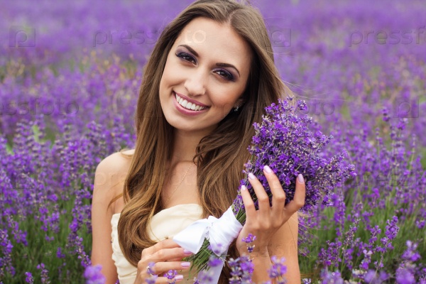 Beautiful smiling woman with nice makeup with bouquet at field of purple lavender flowers