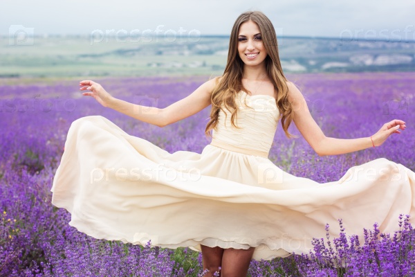 Beautiful smiling woman is wearing wedding dress with flying hair at field of purple lavender flowers
