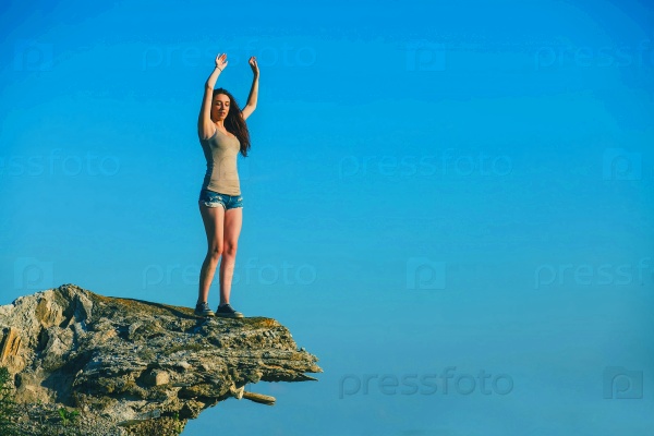 acrophobia tall woman stands on top of a rock cliff edge and is fearful horror