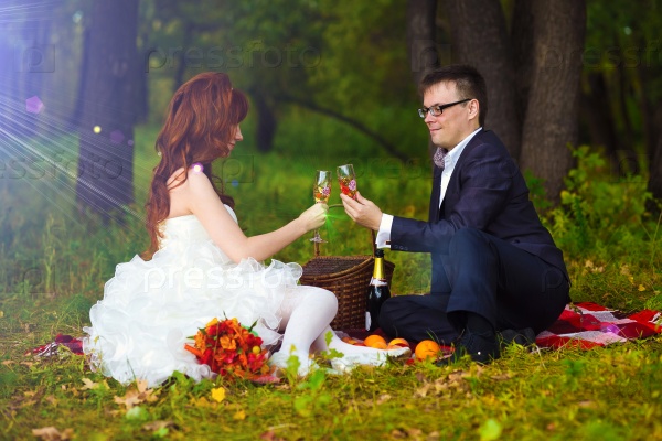 newlyweds couple bride, and groom Russia sitting on green grass, picnic in woods at wedding drink wine