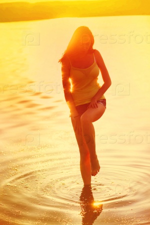 sunlight silhouette of a young beautiful woman girl at sunset on the beach in the water sea ocean