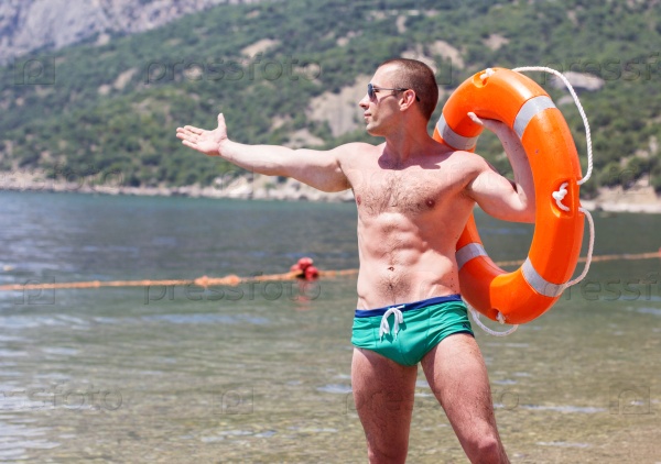 Sexy young man body builder with six pack is posing on the beach with orange lifebuoy ring