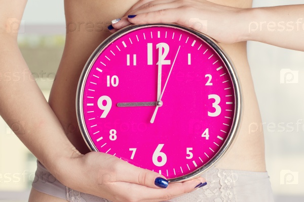 Biological clock ticking - woman holding clock in front of stomach. Pink clock in female hands. toning