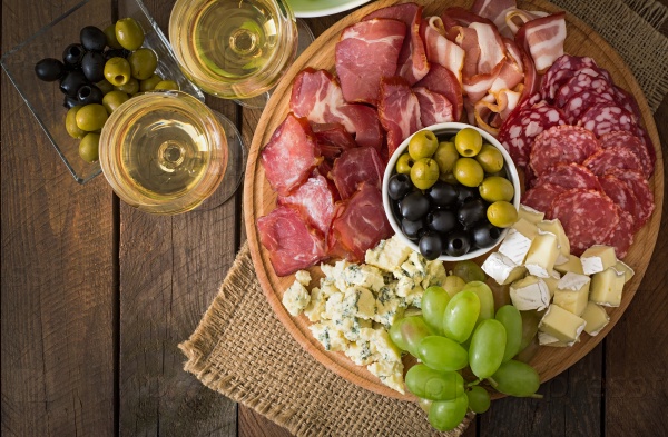 Antipasto catering platter with bacon, jerky, salami, cheese and grapes on a wooden background. Top view