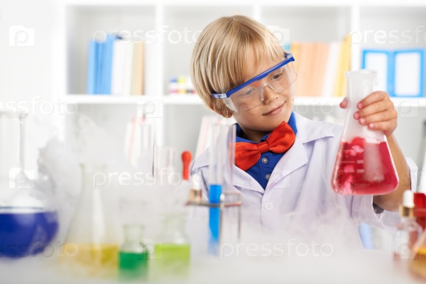 Cute smiling kid looking at the flask with red liquid
