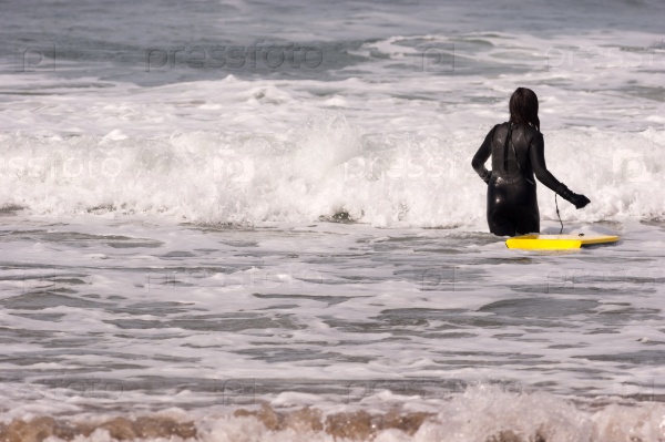 Sports loving person heads out into the surf to ride her board