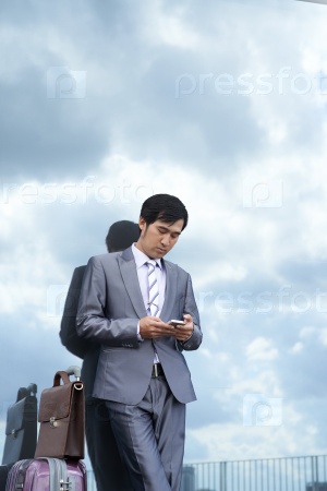 Asian businessman with baggage standing at the mirror wall and texting