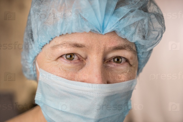 Female doctor wearing medical mask and surgical cap looking at patient and smiling