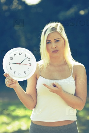 Suspicious\
 attractive young woman with sleeveless blouse pointing time by her finger on a withe big clock concept idea
