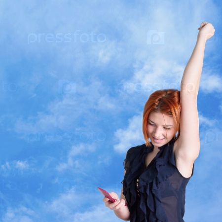 Connect.Happy red-haired girl with mobile phone on a blue sky background.