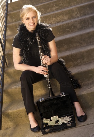 A Female Street Performer Sits on Steps Near Clarinet Case With Tips