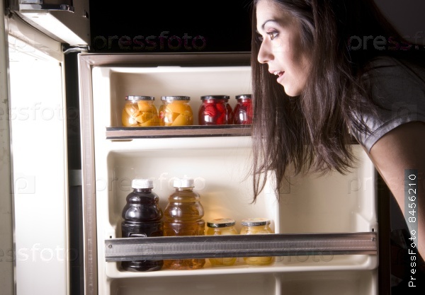 An attractive woman raids the refrigerator late at night looking for a food snack