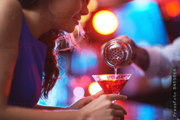 Girl looking at drink in martini glass while barman pouring cocktail for her